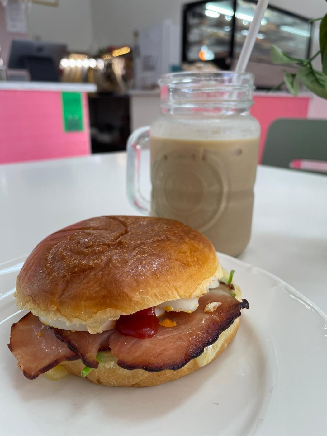 A bacon and egg roll on a white plate with an iced coffee in a jar behind it