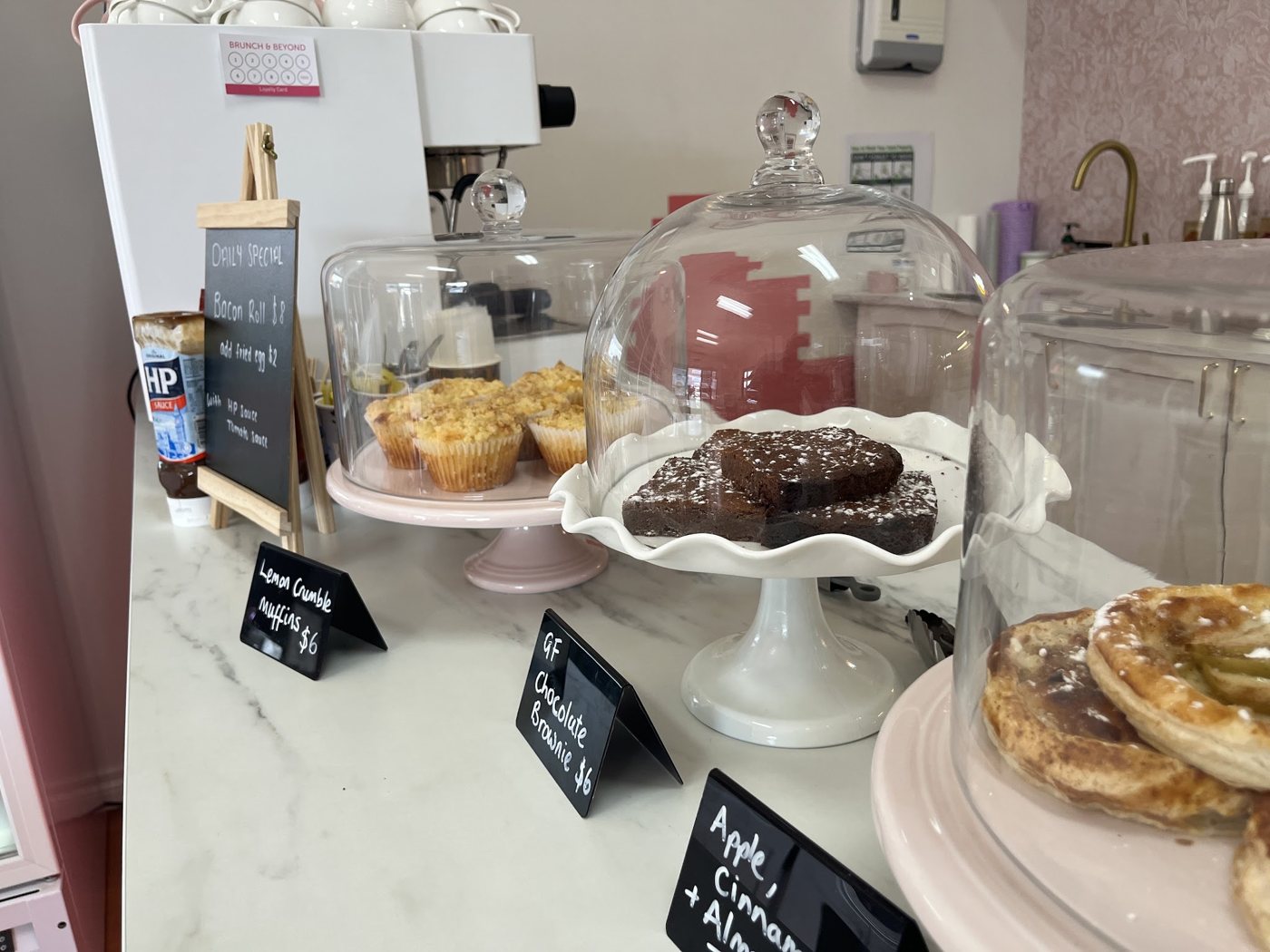 The Brunch & Beyond counter with chalkboard price signs and pastries under glass domes