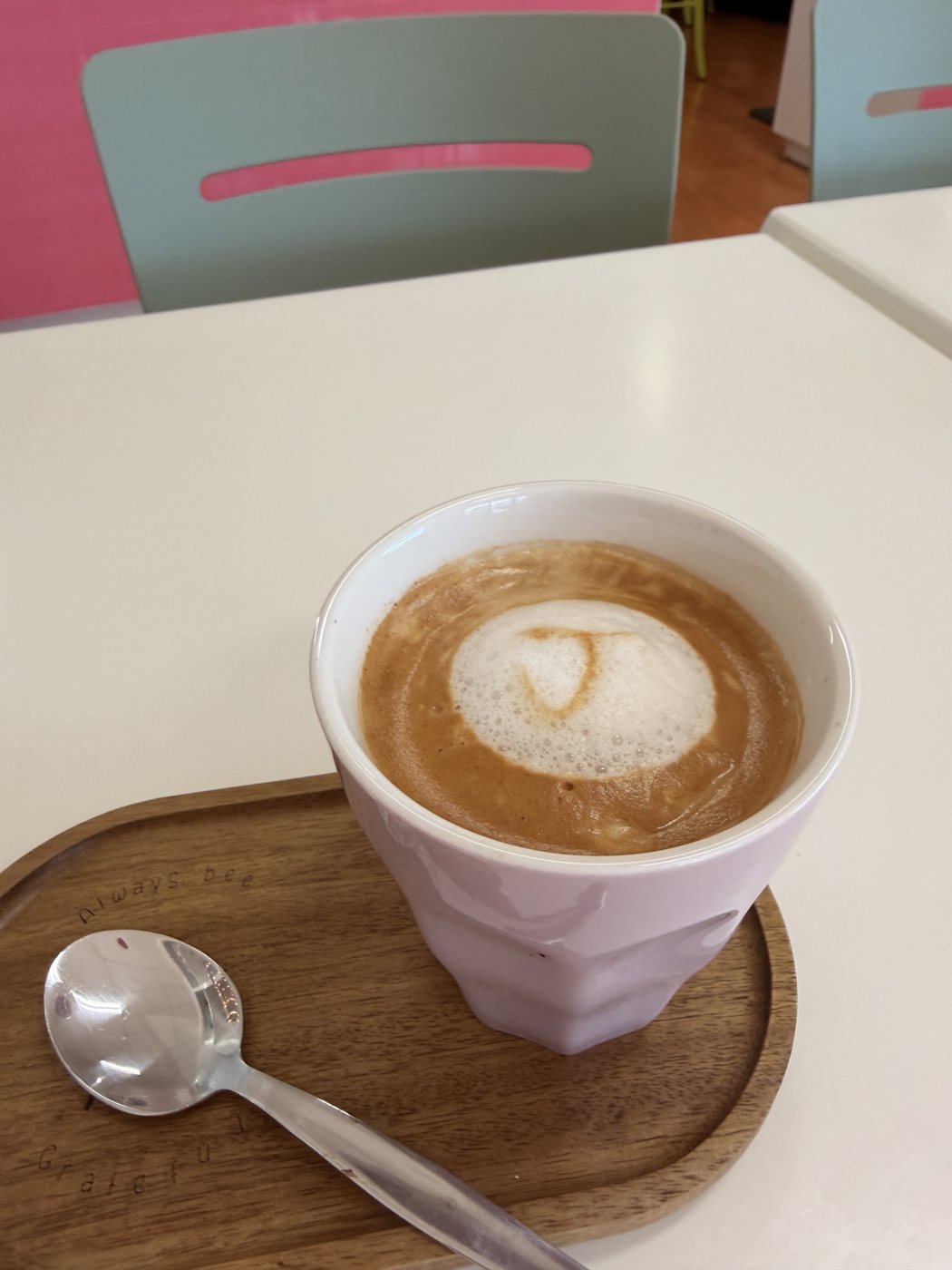 A coffee with a latte-art heart in a pink cup on a wooden tray