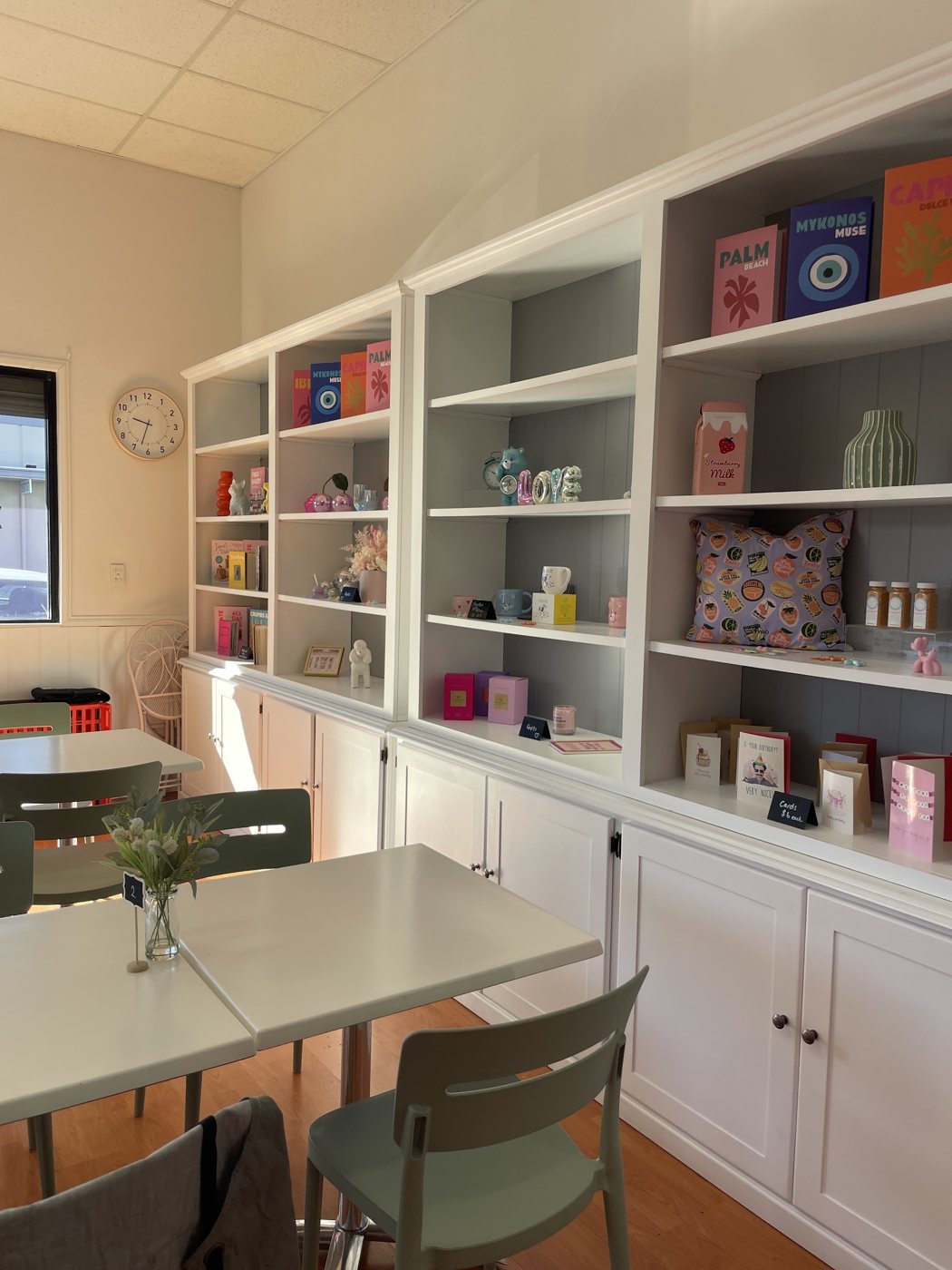 Inside the café: white shelves of cards, candles and homewares beside tables with mint chairs